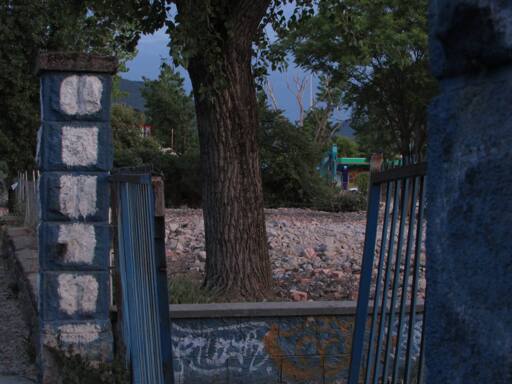 Through an opening in a gate a tree is visible with rubble from demolished buildings behind it.